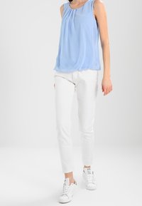 Blusa sin mangas de color azul claro con un diseño drapeado, combinada con pantalones blancos de corte slim y zapatillas blancas. Tejido suave con detalles mínimos.