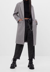 Šedý kabát z vlněné směsi s výstřihem se zářezy, nošený přes černý žebrovaný svetr a černé džíny s vysokým pasem a třásněmi na lemech. Černé kožené boty s masivními podrážkami.