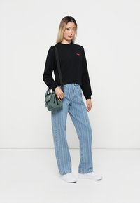 Black long-sleeve shirt with red heart logo, paired with light blue striped high-waisted jeans and a small green crossbody bag. White sneakers.