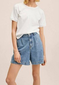 Camiseta de algodón blanca con mangas texturizadas combinada con pantalones cortos de mezclilla azul de cintura alta. Los pantalones cortos tienen un ajuste relajado y costuras visibles.