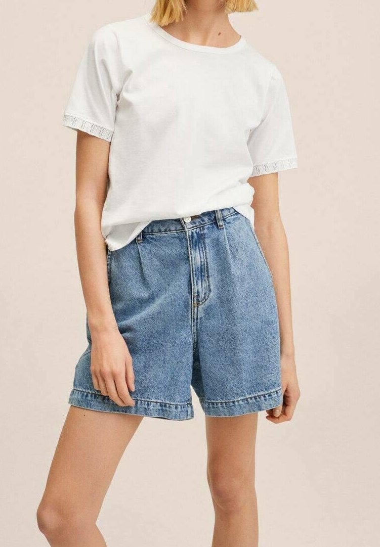 Camiseta de algodón blanca con mangas texturizadas combinada con pantalones cortos de mezclilla azul de cintura alta. Los pantalones cortos tienen un ajuste relajado y costuras visibles.