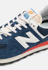 Blue suede sneaker featuring white logo, lightweight construction, padded tongue, contrasting red outsole, and textured mesh accents.