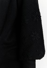 Maglione nero realizzato in un tessuto testurizzato con dettagli in maglia floreale sulle maniche e polsini a costine per una silhouette aderente.
