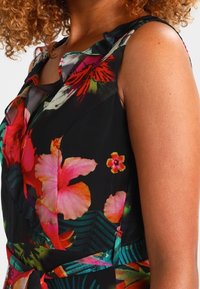 Kwiatowa sukienka na czarnym tle, z intensywnie różowymi i zielonymi kwiatami. Falbany na ramionach oraz paskiem w talii, który podkreśla sylwetkę.