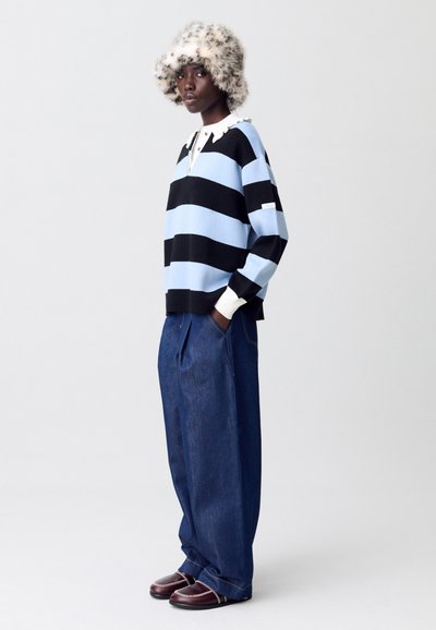 Suéter a rayas con rayas horizontales azul claro y negro, con un cuello blanco y una tapeta de botones. Combinado con pantalones de mezclilla de pierna ancha y zapatos marrones.