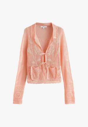 Brzoskwiniowy sweter na szydełku z długimi rękawami, kwiatowymi wzorami, dwoma przednimi kieszeniami i zapięciami na wiązania z przodu.