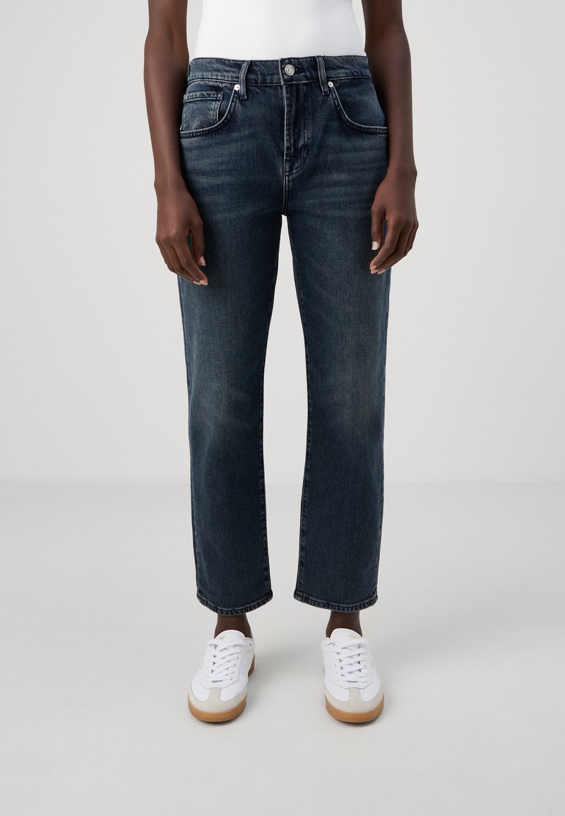 Jeans en denim bleu foncé avec une coupe droite, cinq poches et une fermeture à bouton, associés à des baskets blanches avec des semelles en gomme claire.