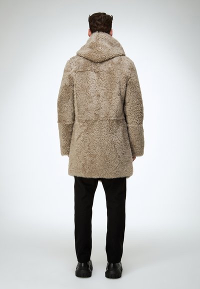 Beżowy, puszysty płaszcz futrzany z kapturem, o luźnym kroju i średniej długości. Noszony na czarnych spodniach i masywnych czarnych butach.