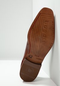 Semelle de chaussure en cuir brun avec des surpiqûres rouges, marquée 'Cuir véritable' et taille '42', présentant une surface texturée et des détails de logo.