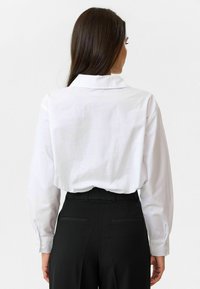 Witte lange mouwen shirt met een kraag, met een relaxte pasvorm. Gecombineerd met zwarte hooggeprijsde broeken, die minimale ontwerpelementen tonen.