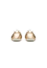Ballerines métalliques dorées avec un bout arrondi, de petits nœuds à l'avant et des semelles en caoutchouc blanc présentant un motif texturé.