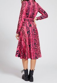 Abito aderente a maniche lunghe di colore rosa con motivi geometrici e floreali neri, gonna svasata e cintura in vita; abbinato a stivaletti neri alla caviglia.