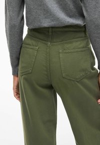 Pantaloni olive green a vita alta con due tasche posteriori, design strutturato e tessuto morbido; abbinati a un top grigio a maniche lunghe.