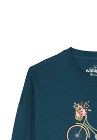 Teal langemouwenshirt met een fietsafbeelding en een rieten mand vol met roze bloemen en groen. Zacht, katoenen materiaal.