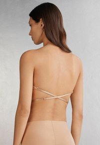 Naked ryggband bh med justerbara korsremmar, tillverkad av slätt tyg, som visar en sömlös design och minimal hårdvara.
