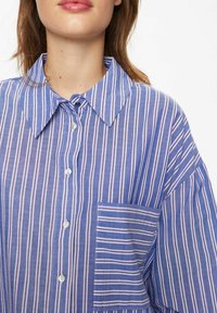 Blue striped shirt made of lightweight fabric, featuring a button-down collar, front pocket, and horizontal and vertical stripes in varying widths.