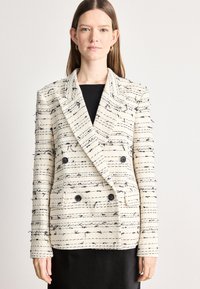 Διπλή μπλούζα σε κρεμ απόχρωση με μαύρες υφασμάτινες ρίγες, διαθέτοντας δύο μεγάλους κουμπιά και φθαρμένα σημεία. Προσαρμοσμένη εφαρμογή με σχέδιο στους γιακάδες.