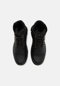Botas negras hasta el tobillo con un exterior de cuero suave, forro interior acolchado y acentos metálicos en los cordones, además de una cremallera lateral para un fácil acceso.