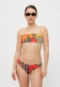 Barevné bikiny s bandeau vrškem a vysokými nohavičkami, zdobené odvážným vzorem kaktusů a palem v oranžové, žluté a černé barvě.