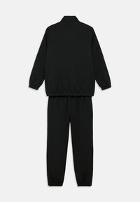 Crni trenirka sastavljena od jakne s patentnim zatvaračem i uspravnim ovratnikom te elastičnim manžetama, i odgovarajućih hlača s elastičnim pojasom i manžetama.