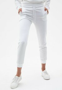 Białe jogger pants z miękkiego materiału, z dopasowanym krojem, elastycznym pasem z sznurkiem i ściągaczami na kostkach. W połączeniu z białymi trampkami.