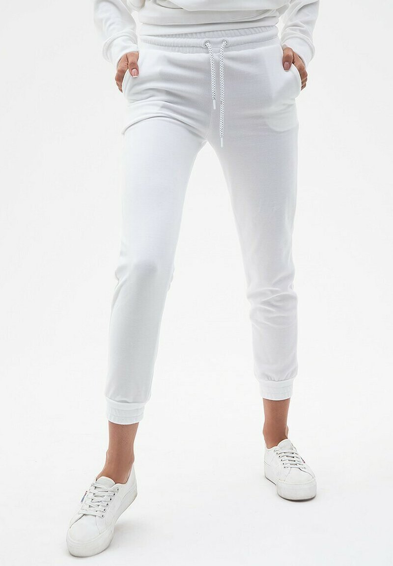 Białe jogger pants z miękkiego materiału, z dopasowanym krojem, elastycznym pasem z sznurkiem i ściągaczami na kostkach. W połączeniu z białymi trampkami.