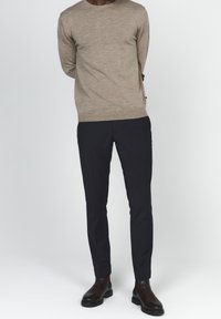 Beżowy sweter z dzianiny z długimi rękawami, w połączeniu z czarnymi, dopasowanymi spodniami i ciemnobrązowymi botkami za kostkę. Gładka faktura i minimalistyczny design.