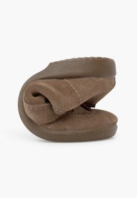 Zapatilla de ante marrón con una textura suave, suela redondeada y un diseño compacto y plegable para facilitar su almacenamiento. Sin herrajes ni acentos visibles.