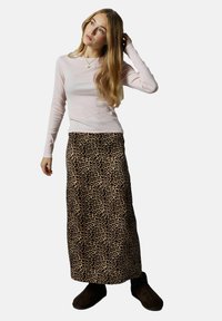 Jupe longue imprimée léopard en tissu doux et texturé ; assortie d'un haut ajusté à manches longues rose clair et de chaussures marron.