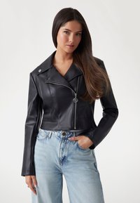 Black faux leather cropped jacket with a notched collar, zippered front, and silver hardware, paired with light blue high-waisted jeans.