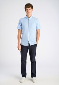 Ljusblå kortärmad skjorta med knappar och bröstficka på vänster sida, i kombination med mörknavy byxor och vita sneakers. Slät tyg, skräddarsydd passform.