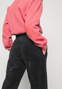 Sweatshirt i mjuk rosa fleece med luftig passform, tillsammans med svarta kordfluwelpants med vertikala ränder och sidofickor.
