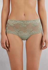 Ropa interior de encaje en un tono verde suave, con un patrón floral a lo largo de la cintura y un tejido suave y opaco en la parte inferior.