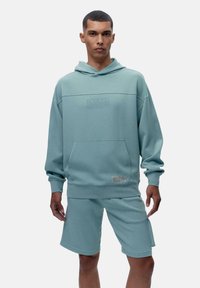 Hele sinine puuvillane kapuutsiga sviiter, millel on eesmine tasku ja graafiline tekst rinnal. Sobib kokku sobivate lühikestega, millel on pehme kangatekstuur.