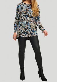 Haut à manches longues avec un motif abstrait multicolore en bleu, beige et noir. Associé à un legging en cuir synthétique noir et des bottines noires.