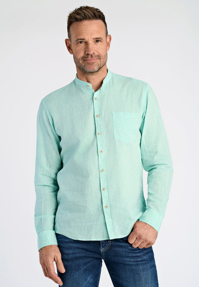 Camicia celeste pallido con colletto alla cinese, maniche lunghe e taschino sul petto, realizzata in un tessuto testurizzato. Abbinata a jeans blu.