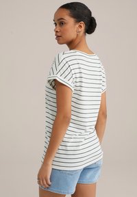 Vit randig t-shirt med gröna ränder, avslappnad passform, uppvikta ärmar och slät textur. Matchad med ljusblå jeansshorts.