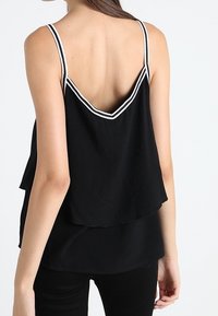 Top senza maniche nero con un design a strati, caratterizzato da una schiena ondulata e cuciture bianche lungo le spalline. Tessuto dalla texture liscia.