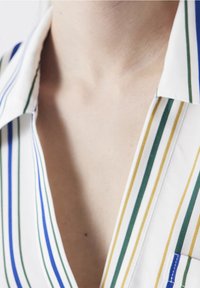 Chemise blanche avec des rayures verticales en bleu, vert et jaune, dotée d'un col et d'une poche poitrine au motif contrastant.