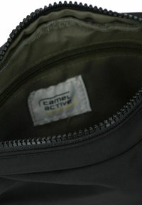 Interno di una borsa nera con zip, rivestito in grigio. Presenta un'etichetta Camel Active e tessuto texturizzato lungo la zip.