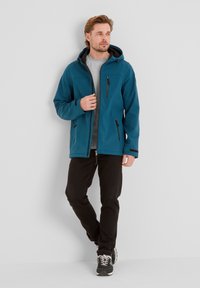 Teal softshell jacket with a hood, front zip, and chest pocket; paired with black pants and sneakers. Smooth texture, lightweight design.