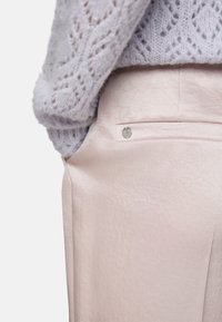 Pink trousers with a smooth texture and a silver button accent on the back pocket, paired with a light purple knitted sweater.