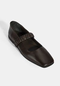 Dunkelbraune Lederflachschuhe mit quadratischer Zehenform und einem strukturierten elastischen Riemen über dem Rist. Glatte Oberfläche und minimalistische Gestaltung.