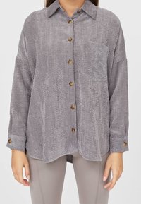 Grå manchester-overskjorta med bröstficka och träknappar, med en avslappnad passform och långa ärmar med mudd detaljer.