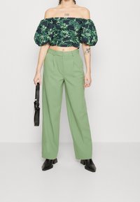 Crop top off-shoulder con motivo floreale scuro e maniche a palloncino, abbinato a pantaloni verdi a gamba larga e alta vita. Borsa nera e stivaletti alla caviglia.