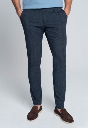 Granatowe spodnie slim fit z delikatnym wzorem teksturowanym, zaprojektowane z bocznymi kieszeniami i gładkim paskiem w talii, zestawione z brązowymi zamszowymi mokasynami.