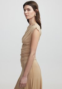 Beige fitted top met gedrapeerde halslijn, korte mouwen en gerimpelde details, gecombineerd met een bijpassende hoge taille rok, met een gladde textuur.