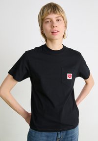 Schwarzes Baumwoll-T-Shirt mit Rundhalsausschnitt und kurzen Ärmeln. Enthält eine Brusttasche mit einem roten Herz-Logo und hat eine glatte Textur.