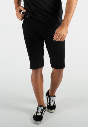 Shorts en denim noir avec des poignets roulés, dotés d'un design classique à cinq poches et d'une ceinture plate. Assortis à des baskets noires et blanches.