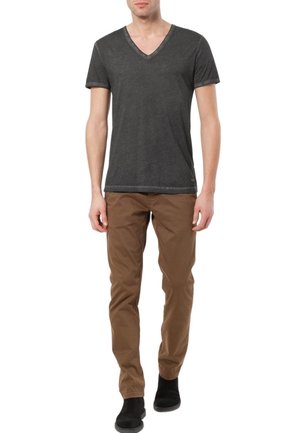 Dunkelgraues V-Ausschnitt-T-Shirt mit kurzen Ärmeln, kombiniert mit braunen Chinos und schwarzen Knöchelstiefeln, vor einem neutralen Hintergrund.